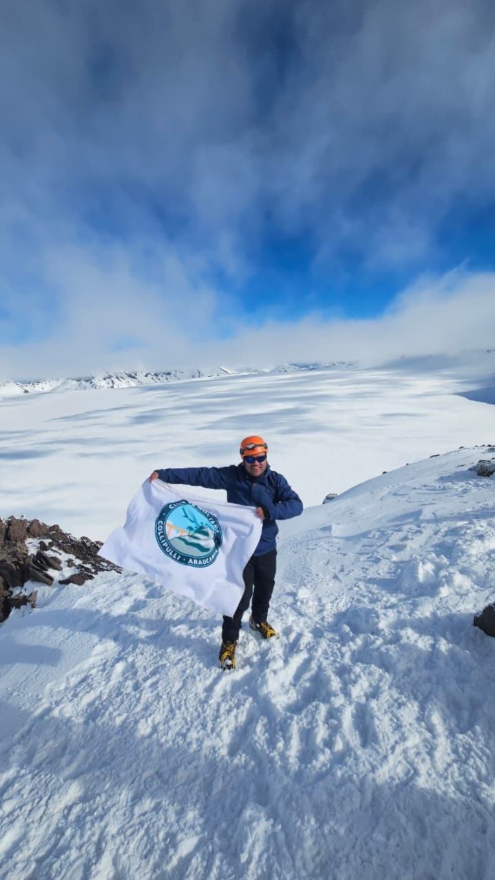 Juan Ulloa sosteniendo la bandera del club en una cumbre nevada